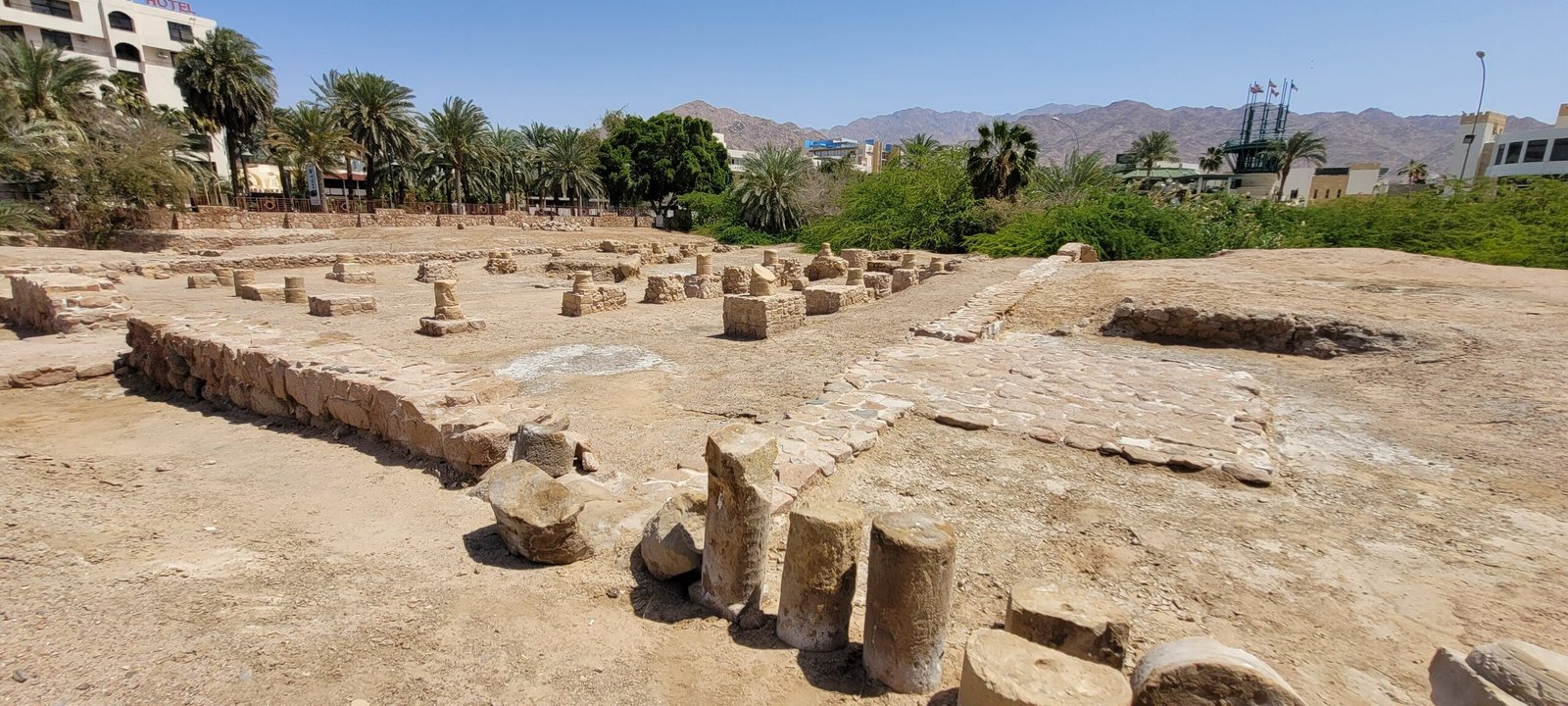 The excavated foundations and column drums of the early Islamic city of Ayla in Aqaba, palms and mountains behind.