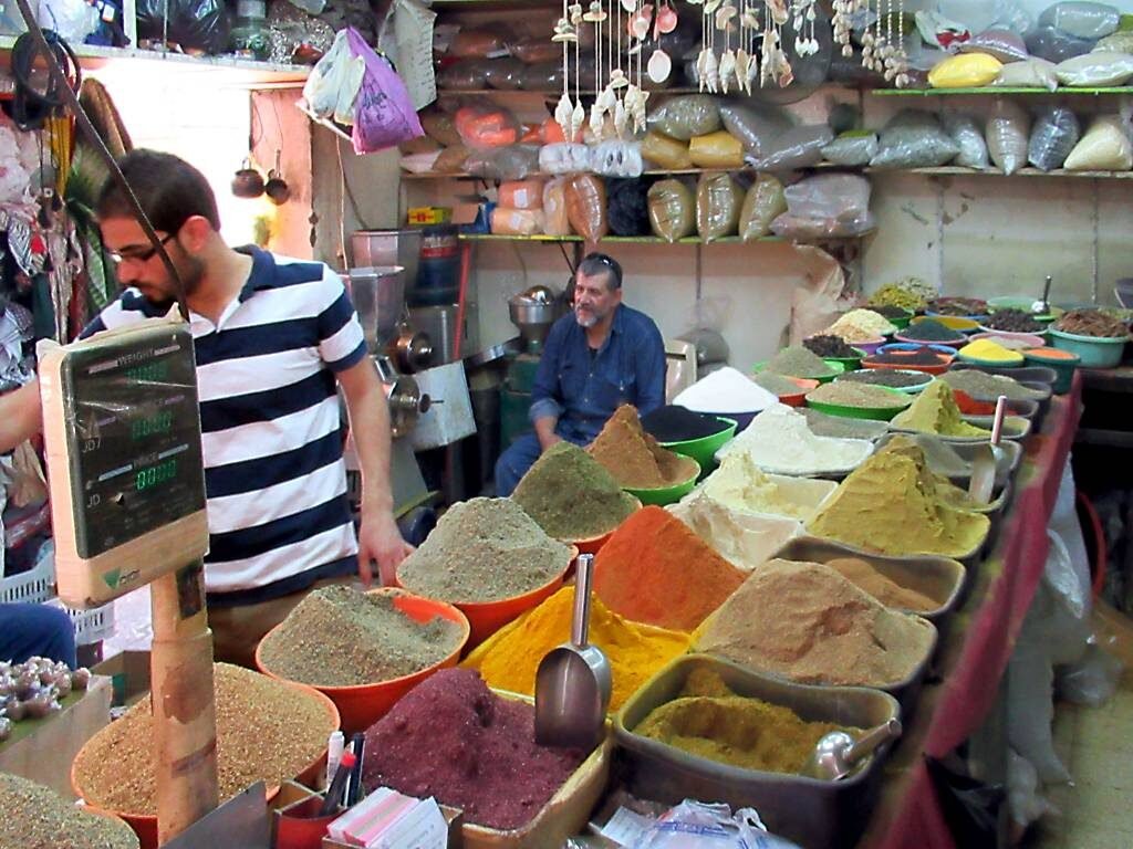 Cones of coloured spices in wide bowls at a spice stall in the Aqaba market, with the shopkeepers behind.