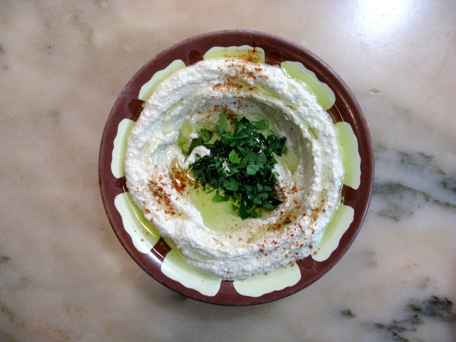 A plate of hummus dressed with olive oil and parsley.