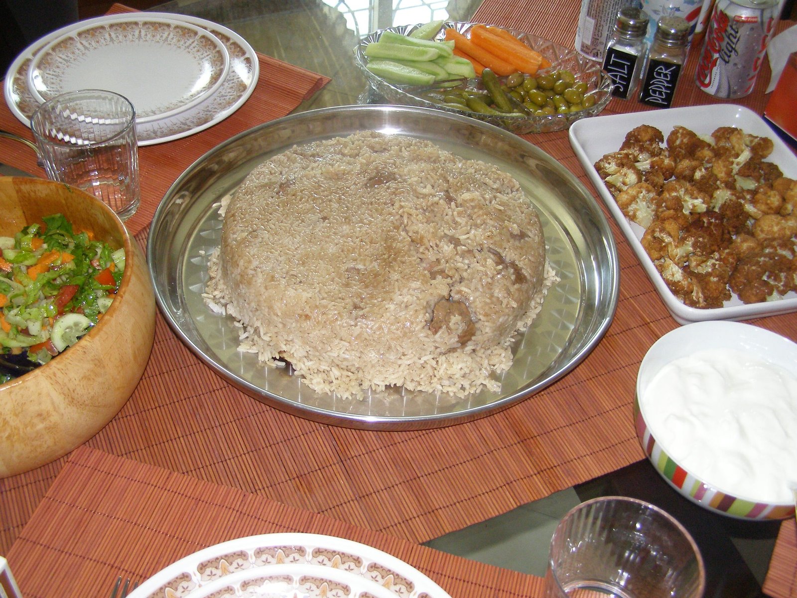 A plate of maqluba - rice, aubergine and chicken turned out of the pot upside down - with yoghurt and salad beside it.
