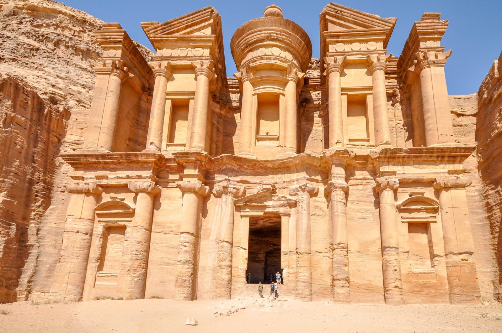 The Monastery, Ad-Deir, carved into a rock face at Petra with small figures at its base for scale.