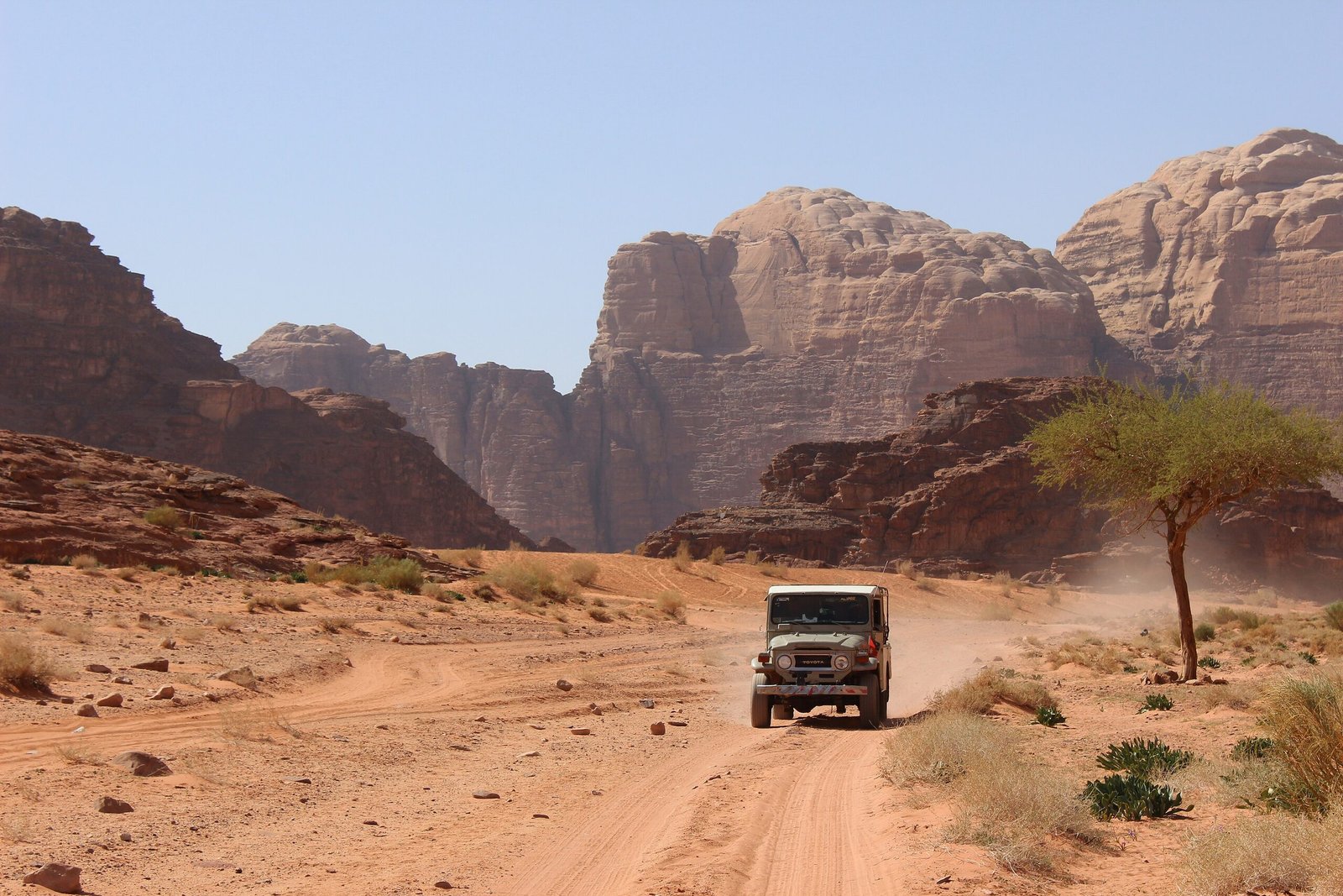 Four-wheel-drive vehicle raising dust on a sandy track between sandstone formations in Wadi Rum.