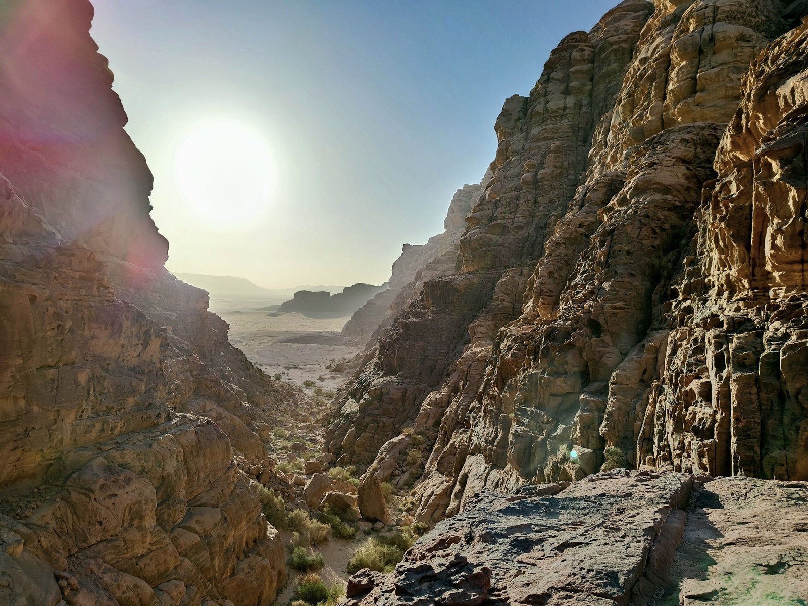 Sunlight bursting over the rim of a narrow rock canyon looking out across Wadi Rum.
